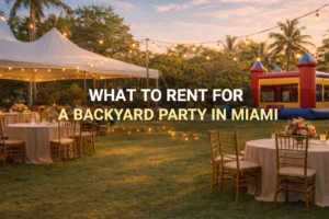 Backyard party setup in Miami with a white event tent, string lights, round tables with chairs, and a colorful inflatable bounce house on a grassy lawn.